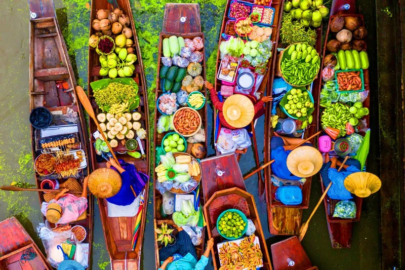 Vendors in traditional hats rowing produce boats through Damnoen Saduak floating market on a Bangkok Thailand tours floating market day trip