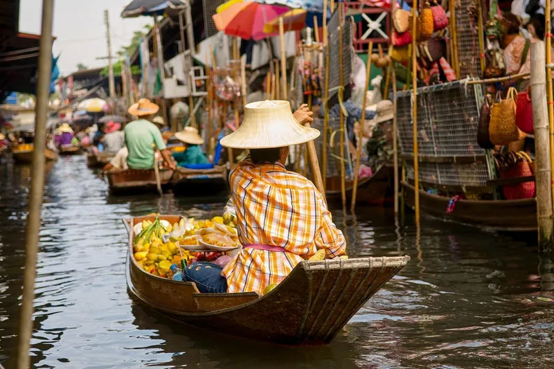 A local commuter train passing through Maeklong Railway Market with vendors pulling back stalls on a Bangkok Thailand tours market day trip