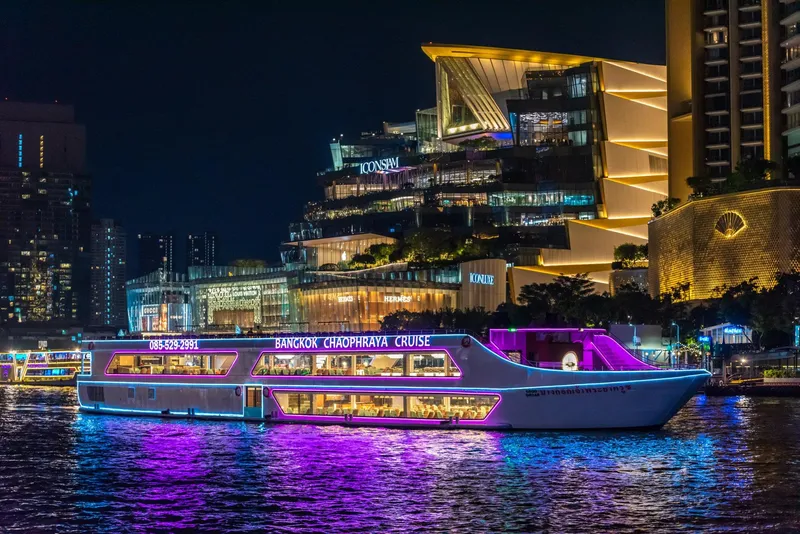 Luxury cruise boat lit up at night on the Chao Phraya River with illuminated Wat Arun in the background on a Bangkok river cruise, Thailand