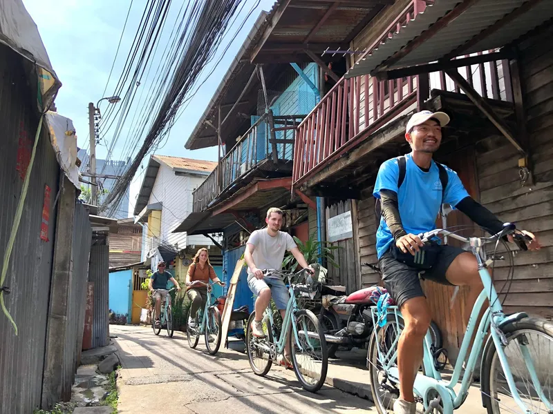Small cycling group riding along a quiet Bangkok canal path past wooden temples and traditional homes on a Bangkok Thailand tours bike tour