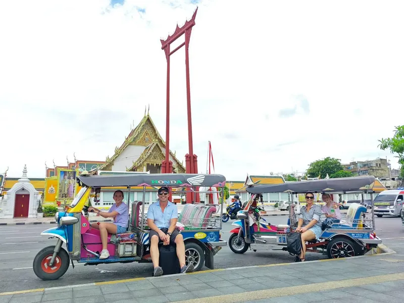 Bright orange tuk tuk speeding past a golden Buddhist temple with tourists aboard on a classic Bangkok tuk tuk tour, Thailand
