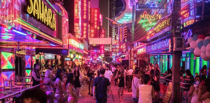 Bright neon signs lighting up Soi Cowboy at night with a tour guide and group walking the entertainment strip on a Bangkok Thailand tours nightlife experience