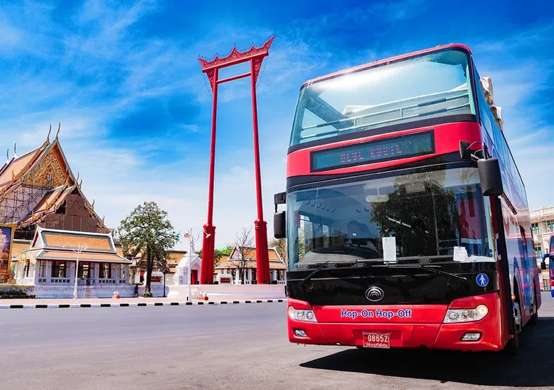 Open-top double-decker hop-on hop-off bus passing the Grand Palace on a Bangkok Thailand tours sightseeing route